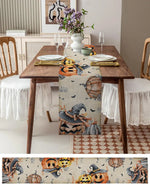 Une table de salle à manger rustique décorée pour l'Halloween avec un chemin de table imprimé de citrouilles, de chauves-souris et d'éléments d'automne.