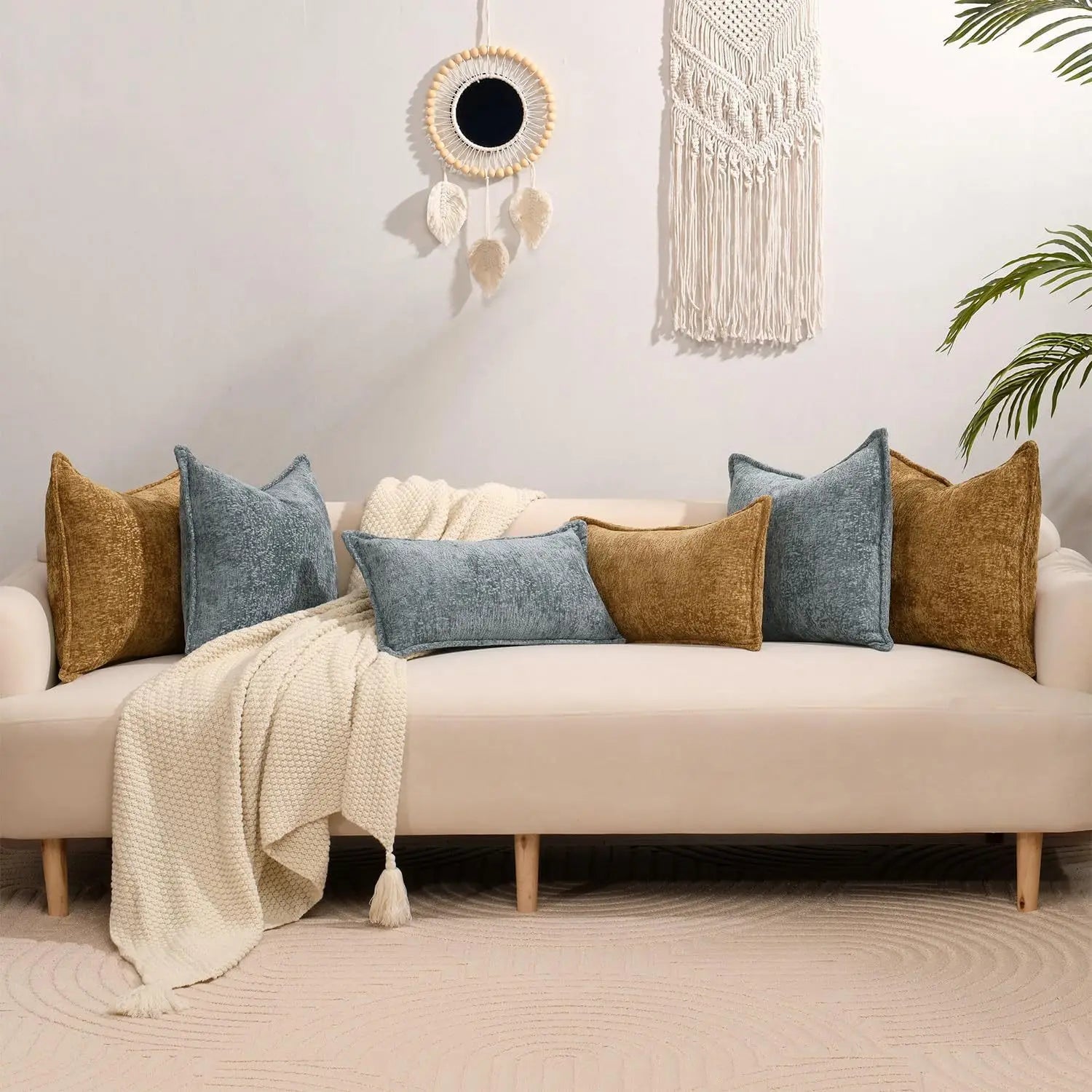 Un aménagement de style bohème avec un canapé douillet orné de coussins et de plaids en tons neutres, complété d'une suspension lumineuse et d'une tenture murale macramé, créant une ambiance cocooning et relaxante.