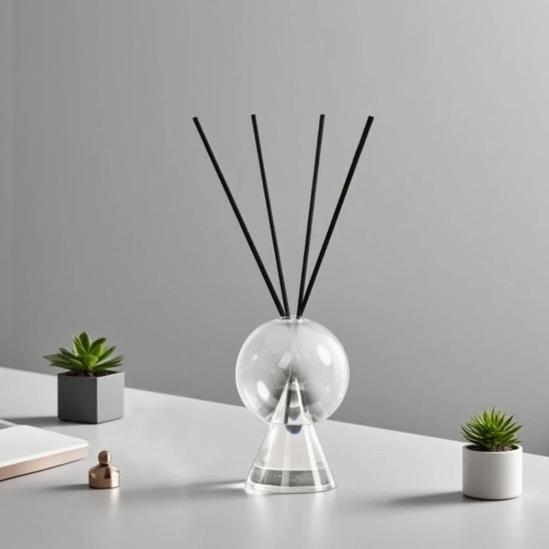 vase verre transparent diffuseur aromates socle triangulaire bâtonnets noirs plante pot blanc livres table