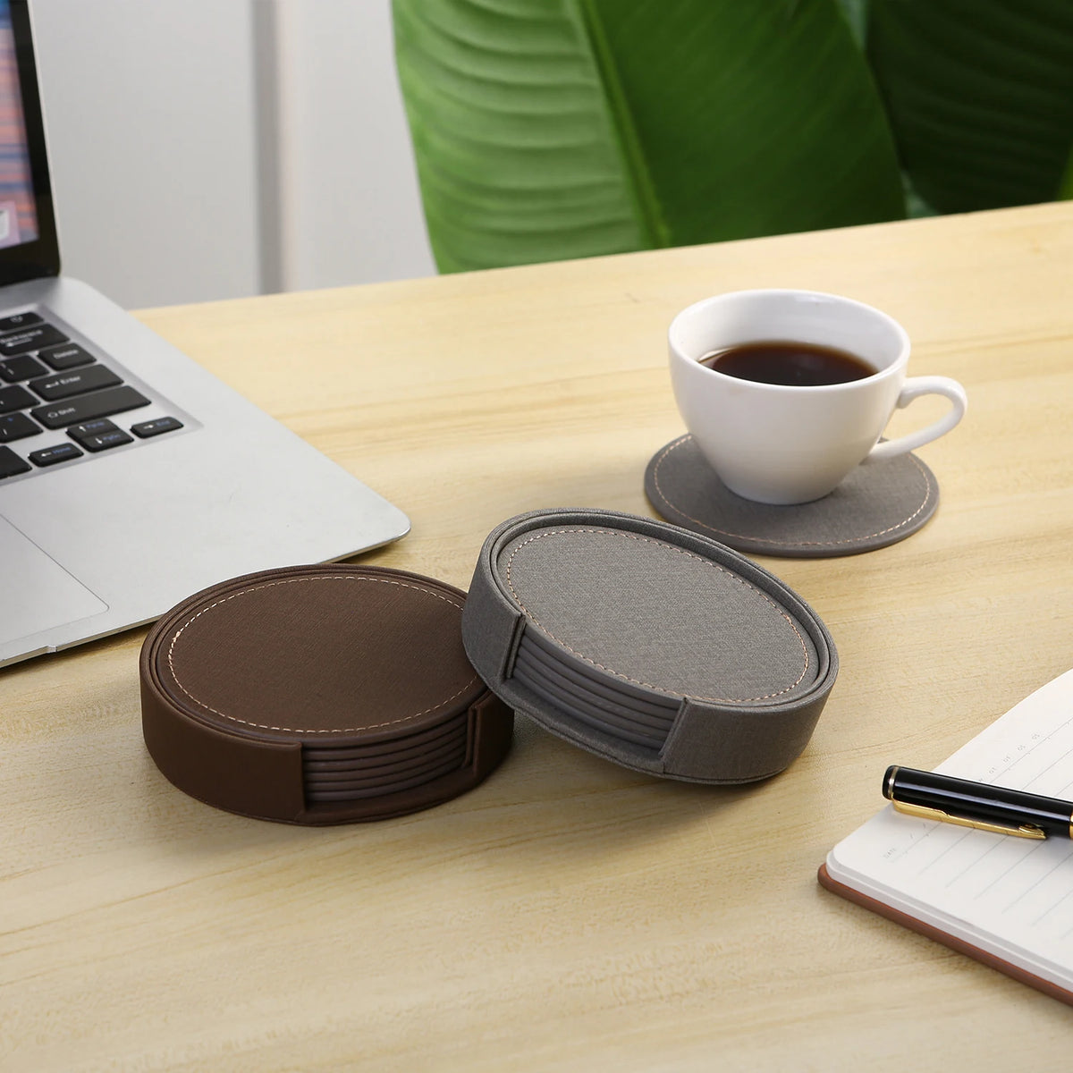 Sur un bureau en bois se trouvent un ordinateur portable, une tasse de café et un ensemble de sous-verres en cuir de différentes couleurs, formant un espace de travail confortable et professionnel.