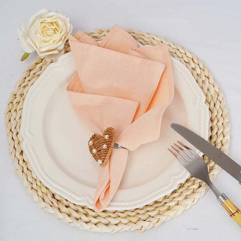 La table de dîner avec une nappe en osier tressé, des serviettes de table peche, une belle rose blanche et des couverts élégants crée une ambiance chaleureuse et raffinée.