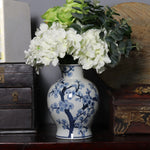 Vase en porcelaine bleu et blanc orné de motifs floraux, contenant un bouquet de fleurs blanches et vertes sur une ancienne armoire en bois.