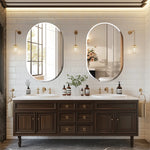 Magnifique salle de bain avec deux grands miroirs ovales encadrés de luminaires dorés, un meuble-lavabo en bois foncé avec de nombreux tiroirs et portes, et une déco végétale apportant une touche naturelle.