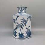 Vase en porcelaine blanc et bleu décoré de motifs tropicaux avec des palmiers, des plantes et des fleurs stylisés.