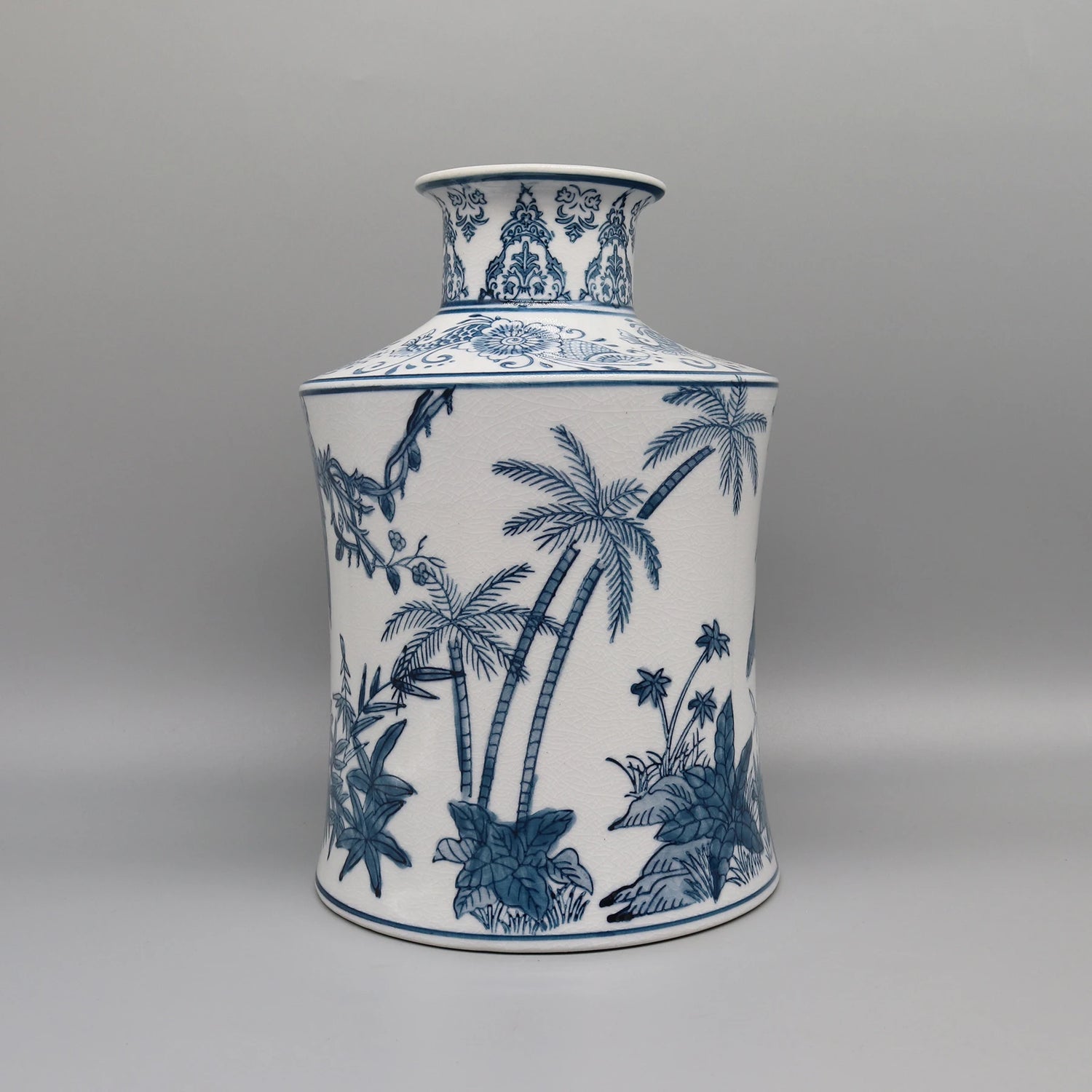 Vase en porcelaine blanc et bleu décoré de motifs tropicaux avec des palmiers, des plantes et des fleurs stylisés.