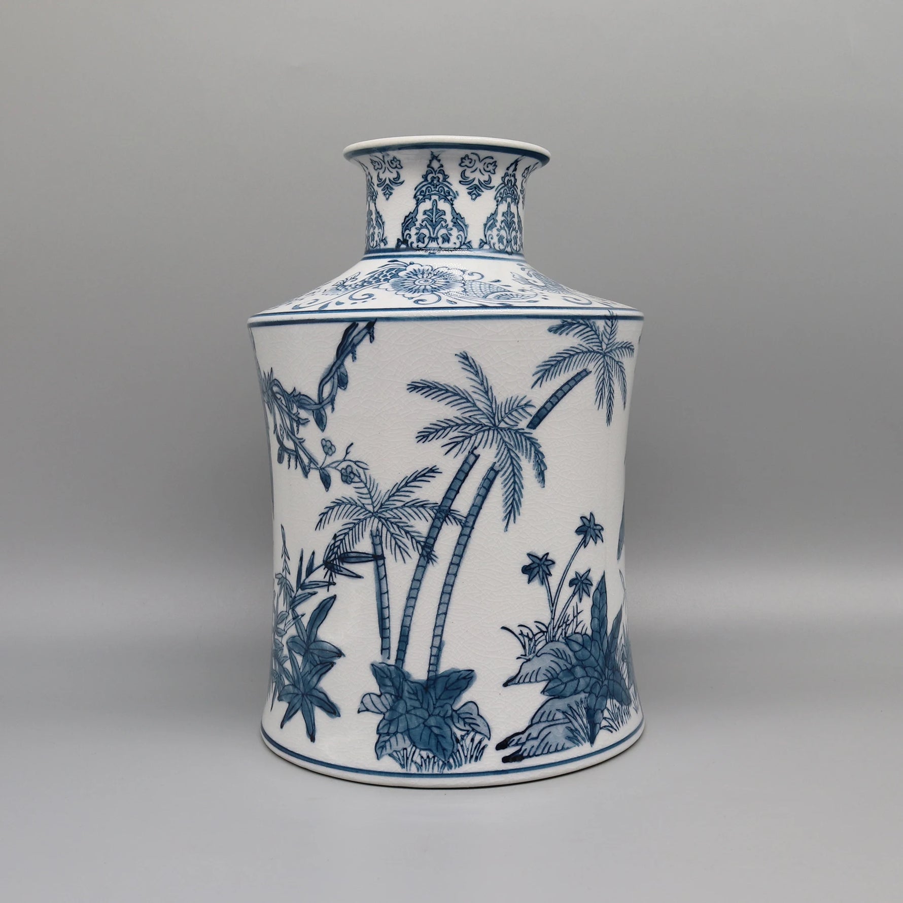 Vase en porcelaine blanc et bleu décoré de motifs tropicaux avec des palmiers, des plantes et des fleurs stylisés.