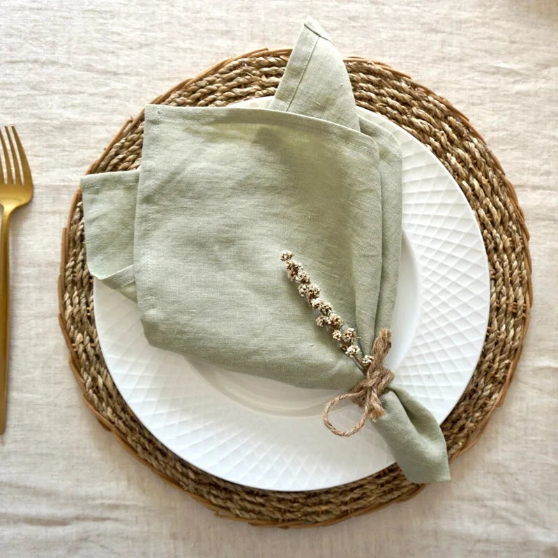 Une serviette de table bleu-vert enroulée avec une décoration de fleurs séchées sur un set de table tressé, placée sur une assiette blanche.