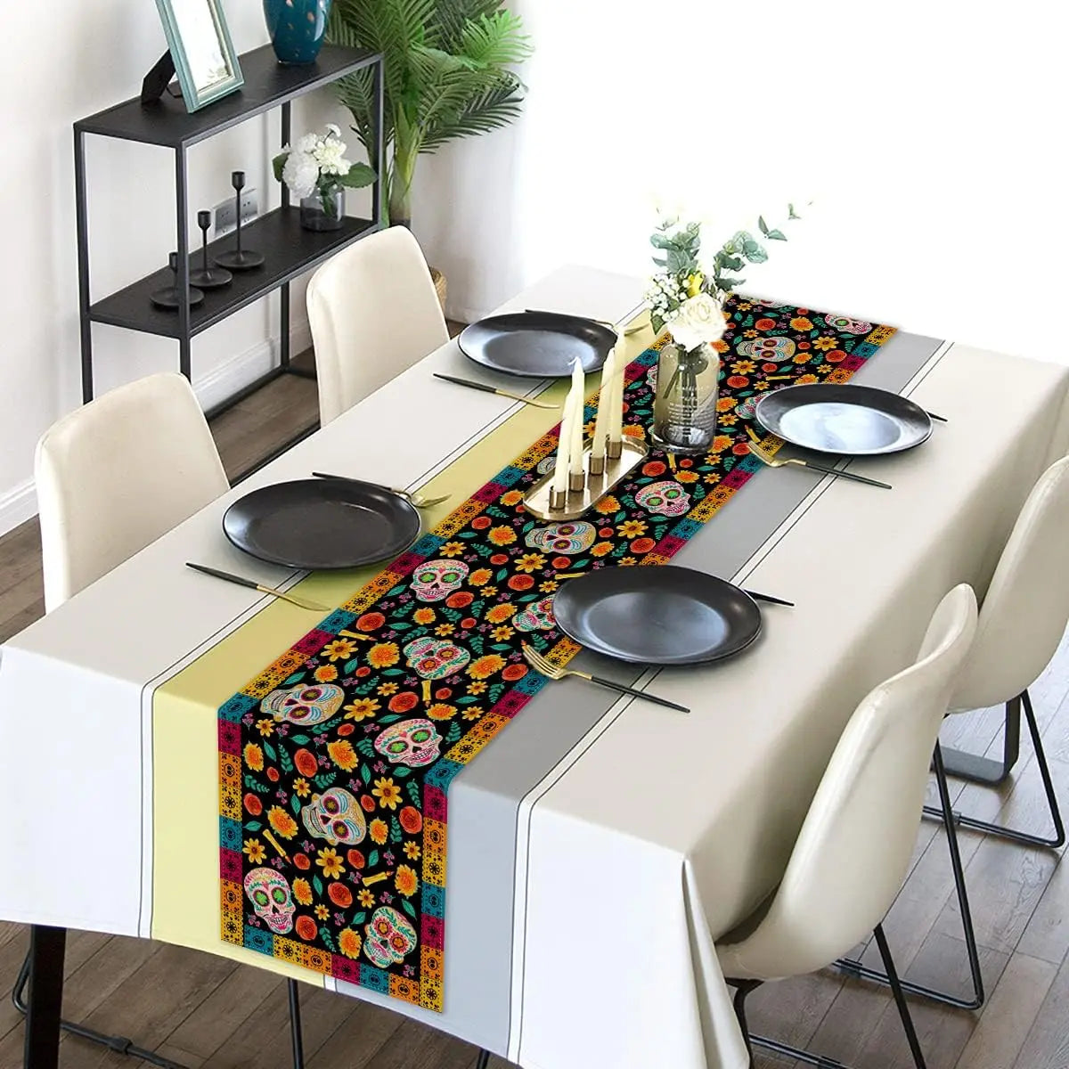 Une table dressée avec des assiettes noires et des bougies sur un chemin de table coloré orné de motifs de crânes mexicains et de fleurs.