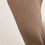 Ceci est une image d'un tissu en tricot marron avec un motif de tressage complexe et répétitif, qui semble être un élément décoratif pour un vêtement ou un accessoire.