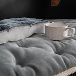 Une tasse de café posée sur une couverture grise et moelleuse, créant une atmosphère de confort et de détente dans un environnement sombre et intime.