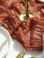 Des nappes en tissu rougeâtre aux plis flottants, ornées d'une élégante bougie d'or, créent une atmosphère chaleureuse et accueillante.