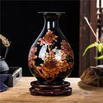 Vase noir orné de fleurs dorées et rouges sur un support en bois, créant une belle décoration d'intérieur rustique.