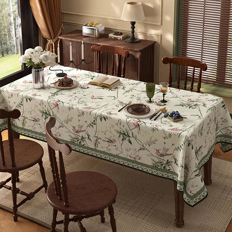 Une magnifique table recouverte d'une nappe ornée de motifs floraux et de papillons, entourée de chaises en bois ancien, créant une atmosphère chaleureuse et raffinée.