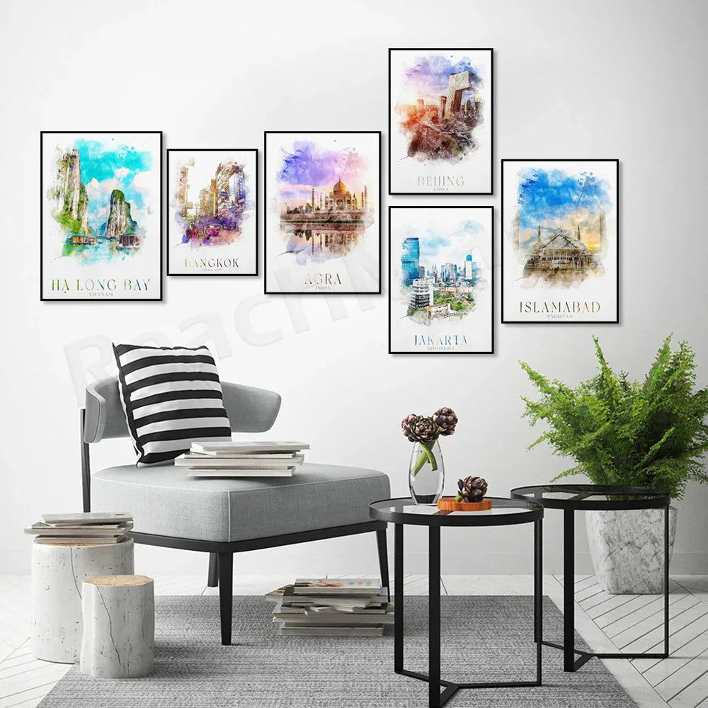 Cette image présente une collection de paysages urbains colorés et aquarellés représentant différentes villes du monde, comme Ha Long Bay, Bangkok, Agra, Jakarta et Islamabad, encadrés sur un mur blanc avec un fauteuil gris, une table basse en marbre et un pot de plante verte.