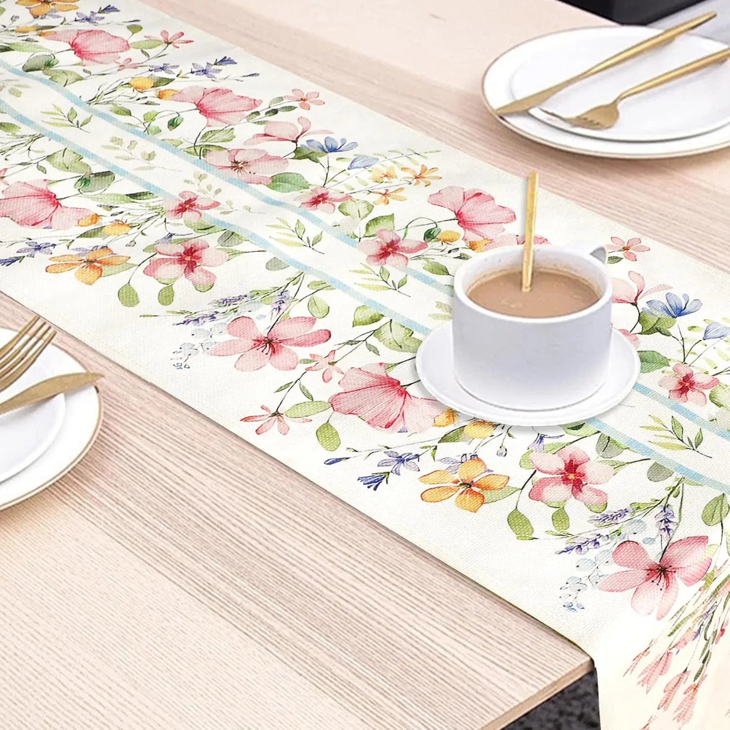 Magnifique chemin de table aux motifs floraux colorés, avec une tasse de café fumante et des couverts en métal doré sur un fond en bois clair.