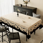 Une table à manger élégante avec un motif floral sur la nappe, ornée de bougeoirs et d'un vase de fleurs, sur un meuble vintage noir dans une pièce lumineuse.