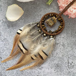Un collier pendentif en plumes marron et beige, décoré de perles et de pierres précieuses, créant une parure naturelle et originale.