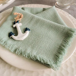 Un linge de table vert pastel avec une décoration ancre marine, créant une ambiance chaleureuse et maritime.