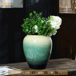 Un vase en céramique de couleur vert décoré avec un bouquet de fleurs blanches et de feuillage vert.