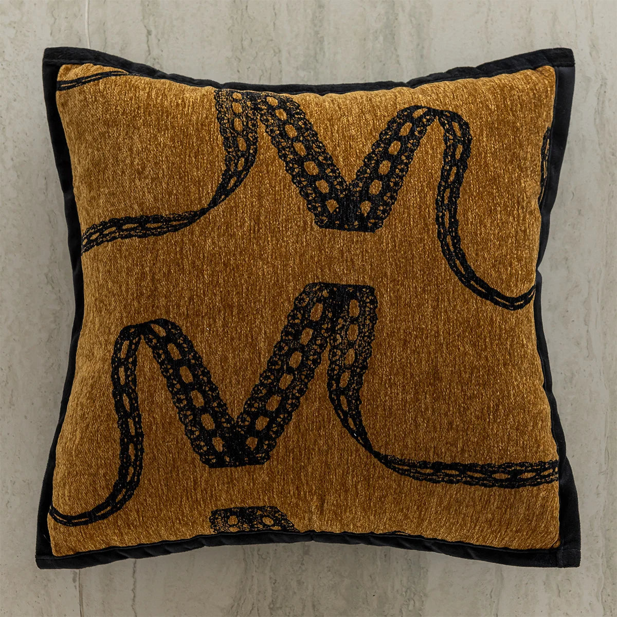 Coussin orné de motifs reptiliens dorés et noirs sur un fond brun ocre.