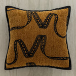 Coussin orné de motifs reptiliens dorés et noirs sur un fond brun ocre.
