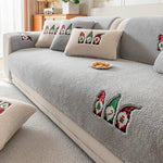 Un canapé gris douillet orné de coussins au motif de petits lutins festifs, une atmosphère confortable et chaleureuse.