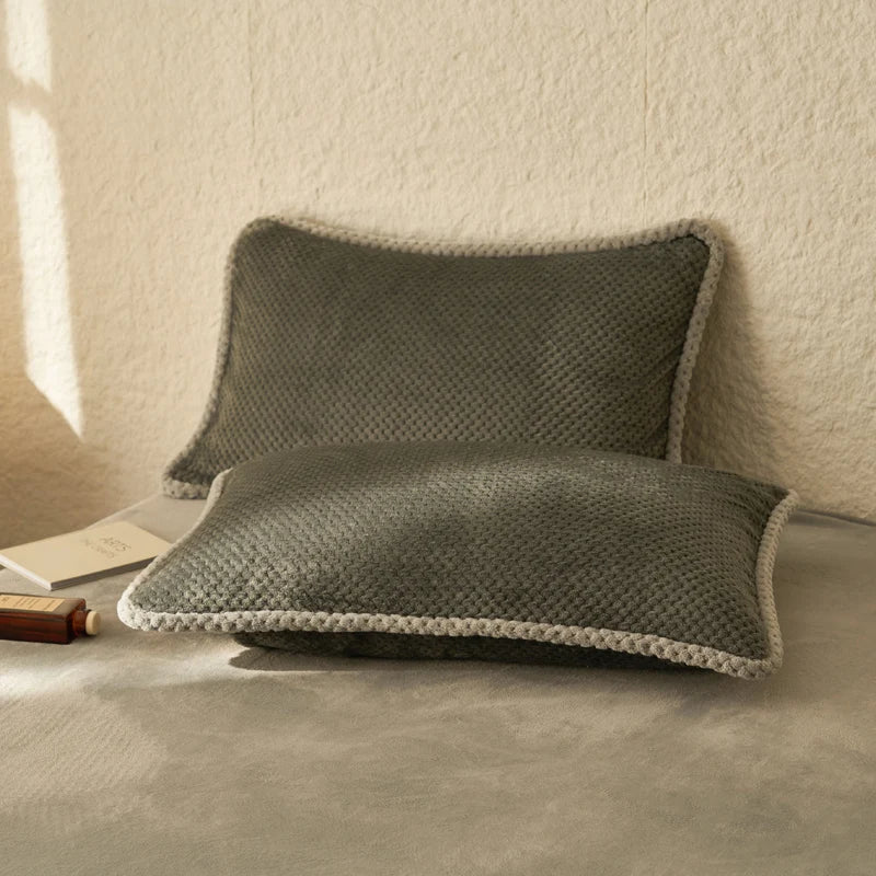 Des coussins gris élégants et confortables, avec un motif en nid d'abeille texturé, posés sur un lit ou un canapé, créant une ambiance chaleureuse et apaisante dans la pièce.