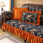 Élégant canapé en cuir brun garni de coussins aux motifs floraux bleu marine et orange, créant une ambiance chaleureuse et raffinée dans cette pièce.