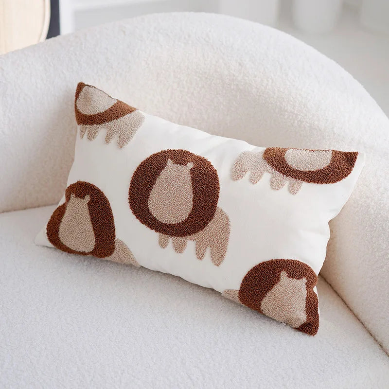 Un coussin blanc et crème décoré de motifs bruns représentant des silhouettes d'oiseaux.