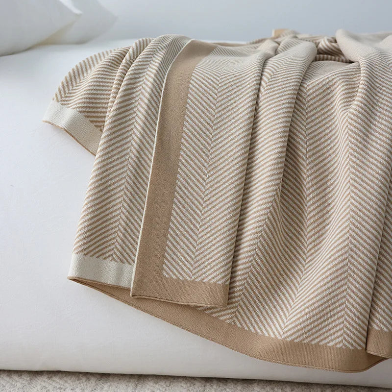 Une couverture en tricot beige et blanc aux motifs chevrons, parfaite pour créer une ambiance cocooning et chaleureuse dans la chambre.