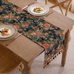 Un chemin de table décoratif aux motifs floraux colorés posé sur une table en bois, accompagné de plats avec des fruits.