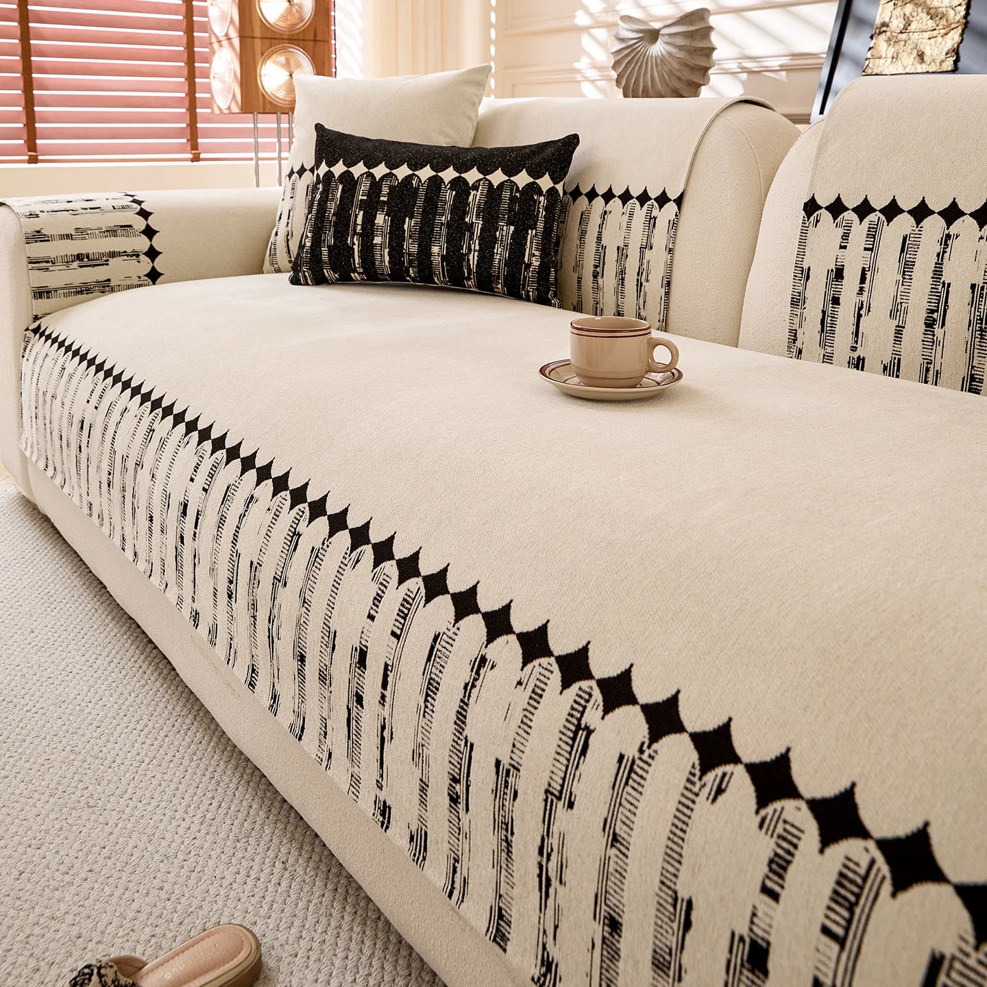 Canapé confortable avec des motifs graphiques noirs et blancs, accompagné d'une tasse de boisson et de décorations d'intérieur dans un style élégant.