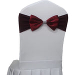 Nœud papillon en velours bordeaux décoré de strass sur une chaise blanche.