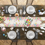 Une belle table de Pâques avec une nappe colorée et des décorations printanières, des assiettes et ustensiles en blanc et noir, et un plat rempli d'oeufs de Pâques multicolores.