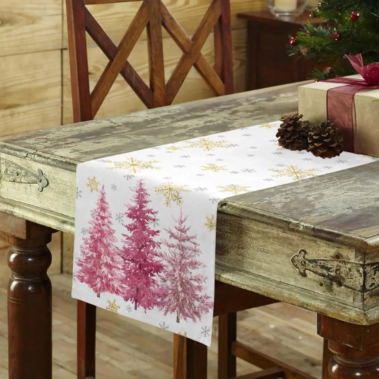 Chemin de table orné de sapins roses et de flocons d'or sur fond de meuble vintage décoré pour Noël.