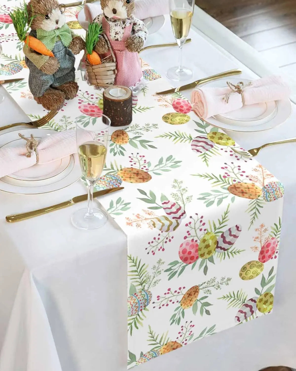 Une scène printanière festive avec des figurines de lapin, des verres de champagne et une nappe décorée de motifs colorés de fleurs, feuillages et œufs de Pâques.