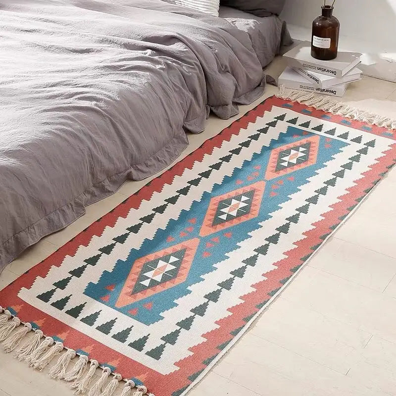 Tapis géométrique multicolore de style aztèque avec des motifs triangulaires et un jeu de couleurs chaudes et froides, posé au pied du lit.
