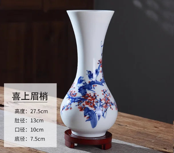 Vase décoratif en porcelaine blanche avec un motif floral bleu et rouge, posé sur un support en bois.