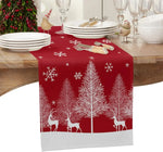 Une table de fête avec une nappe rouge ornée de silhouettes de cerfs et de sapins enneigés sous un ciel étoilé, rappelant l'ambiance festive de Noël.