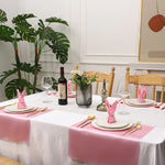 Une table dressée élégamment avec des touches de rose, des verres, des bouteilles de vin et des fleurs, pour un repas chic et raffiné.