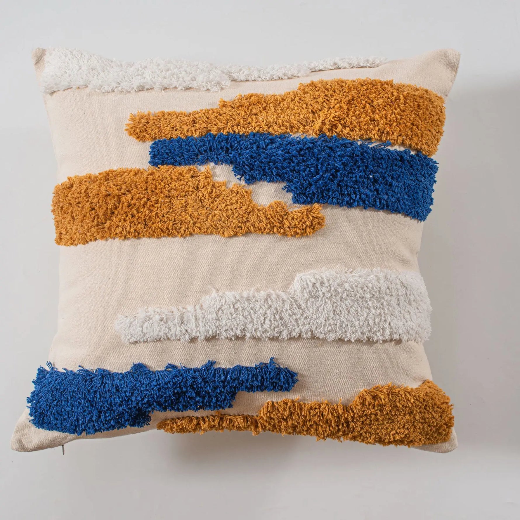 Coussin décoratif avec des bandes texturées bleu et or sur un fond beige, créant un design moderne et sophistiqué.