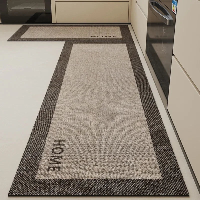 Tapis d'entrée gris avec motifs et inscription "HOME" et "WOHH" visible sur un sol blanc dans une cuisine.