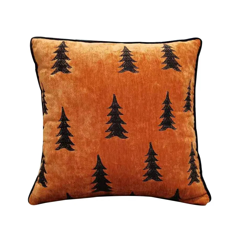 Coussin décoratif orange orné de motifs d'arbres de forêt noirs sur un fond velours.