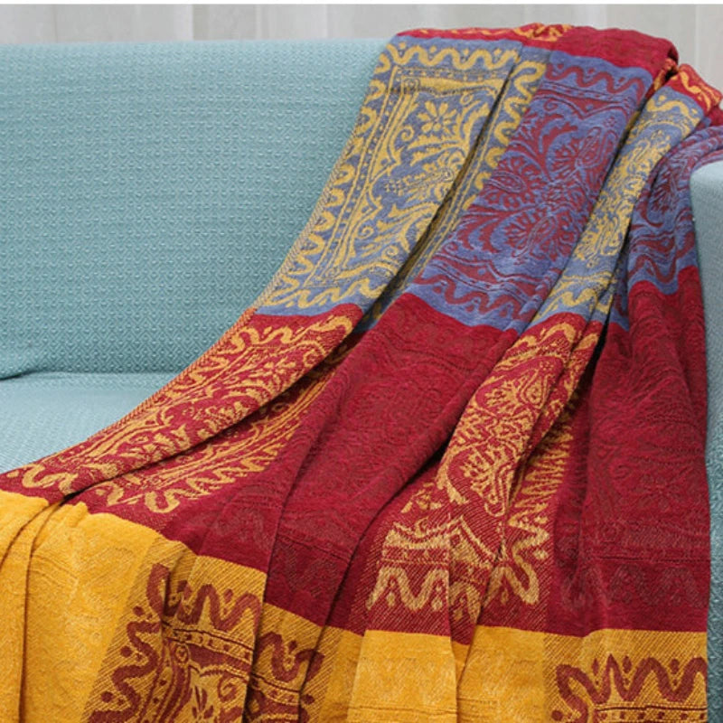 Couverture tissée de motifs colorés et ethniques aux teintes chaudes de rouge, d'or et de bleu, évoquant une atmosphère riche et chaleureuse.