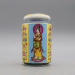 Un pot en porcelaine décorée de motifs et d'une figure de divinité bouddhiste aux vêtements colorés, posé sur un fond gris.