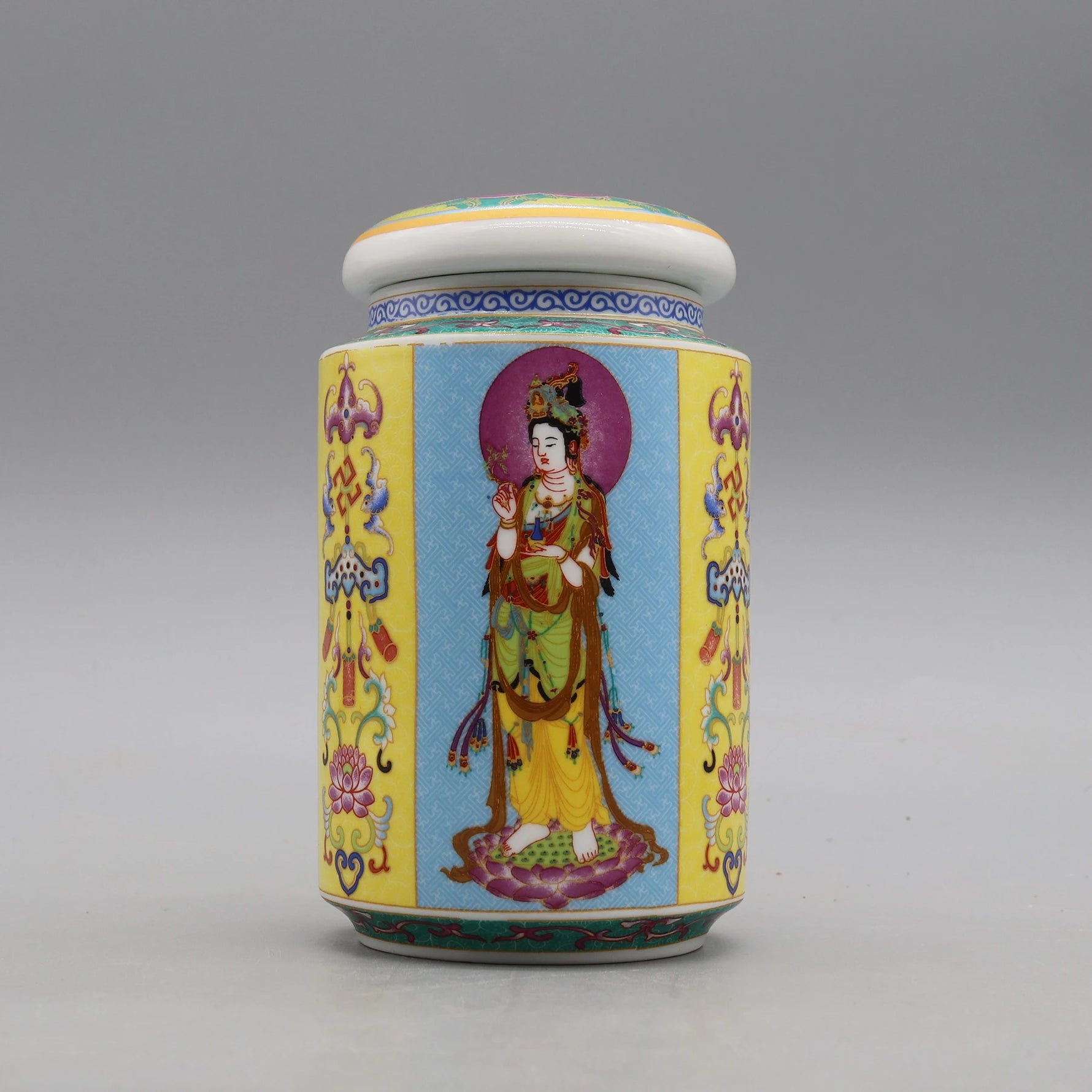 Un pot en porcelaine décorée de motifs et d'une figure de divinité bouddhiste aux vêtements colorés, posé sur un fond gris.