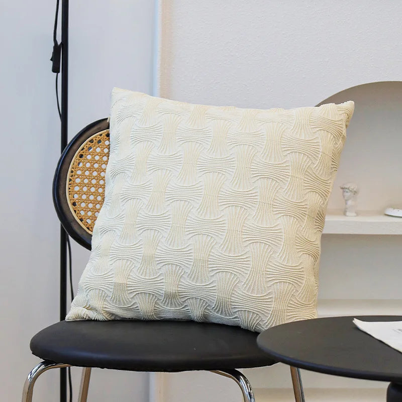 Coussin décoratif blanc ivoire avec un motif abstrait en relief, posé sur une chaise noire dans un intérieur moderne.
