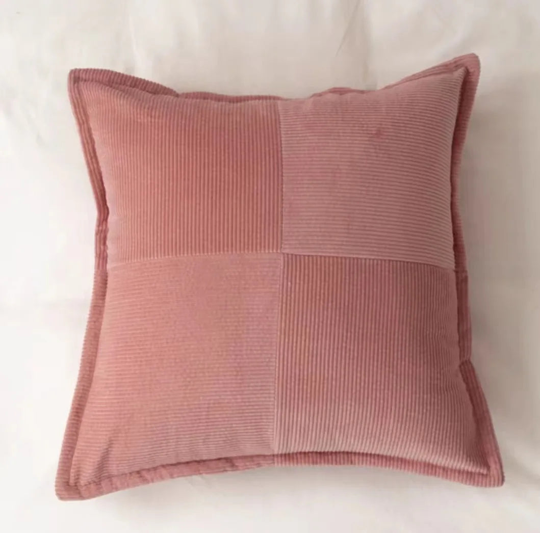Un coussin rose en velours côtelé, avec un motif géométrique contrasté, offrant une touche de douceur et d'élégance à l'espace.