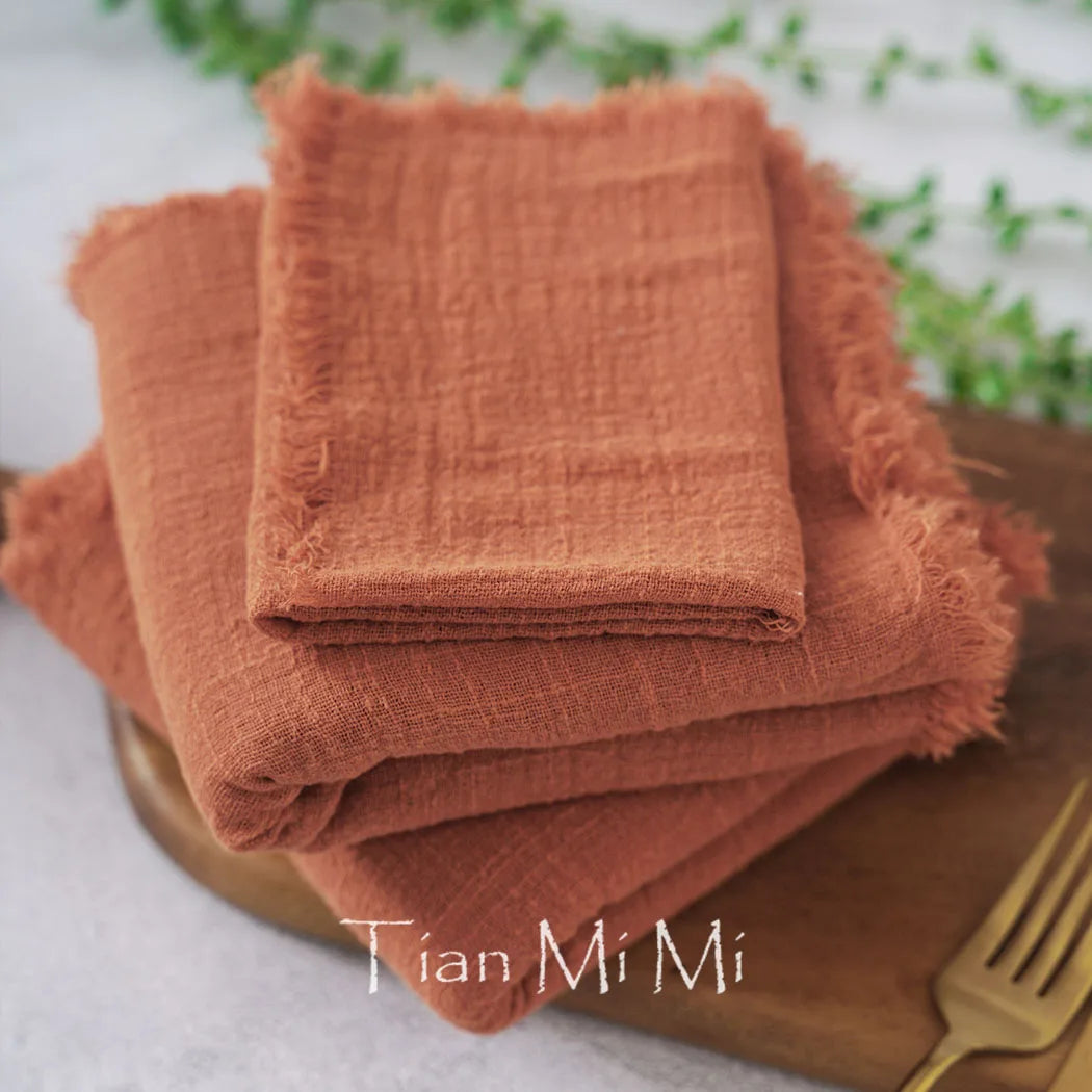 Des serviettes de table en lin orange vif empilées sur une surface en bois, créant une composition naturelle et texturée.
