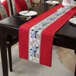 Cette image montre un chemin de table en rouge avec un motif floral bleu et or, posé sur une table en bois sombre, accompagné d'assiettes et de baguettes.
